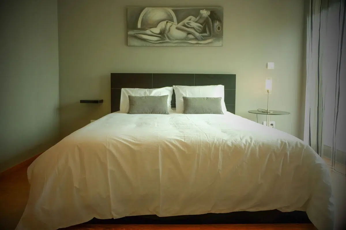Cozy double bedroom with white bedding, grey pillows, dark wood headboard, and a modern art painting at Guest House da Fajã de Baixo